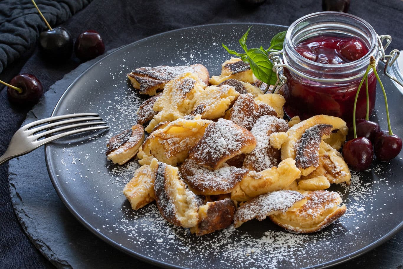 Scrambled pancakes (Kaiserschmarrn) with cherries on a plate and strawberry jam