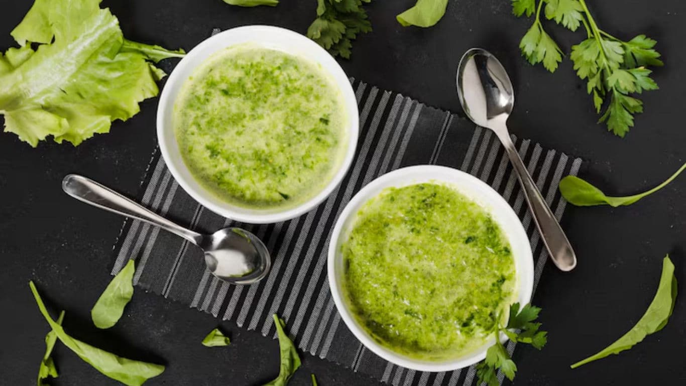Two bowls of green vegetable soup with herbs