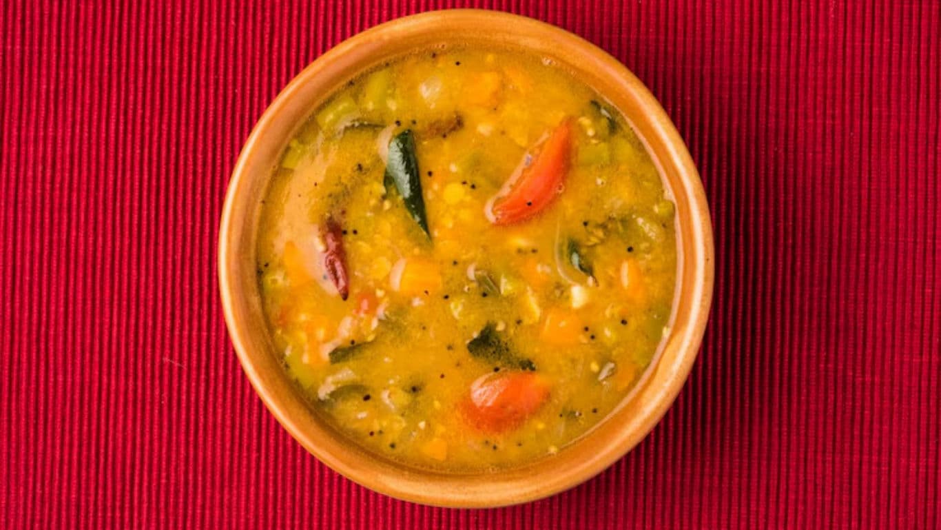 Traditional Indian sambar in wooden bowl on red mat