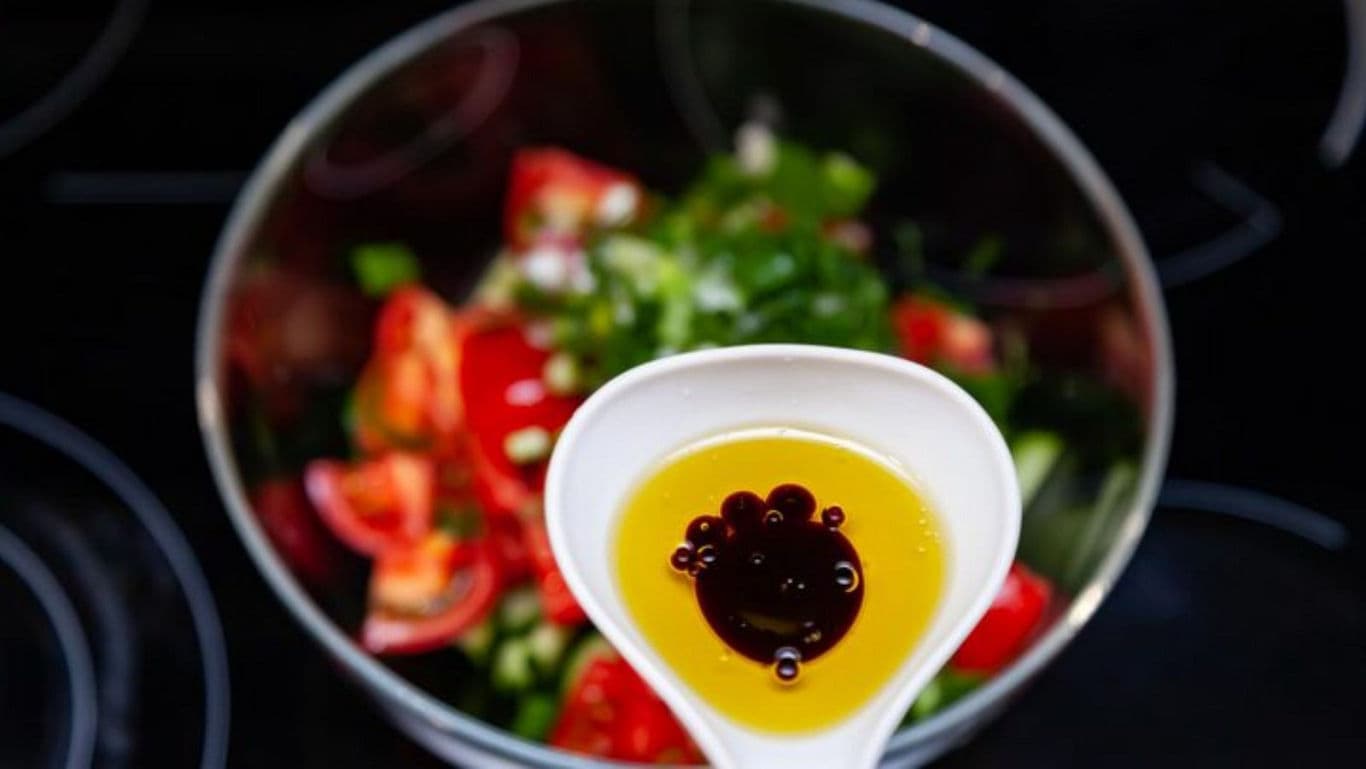 Spoon with oil and vinegar above fresh salad bowl