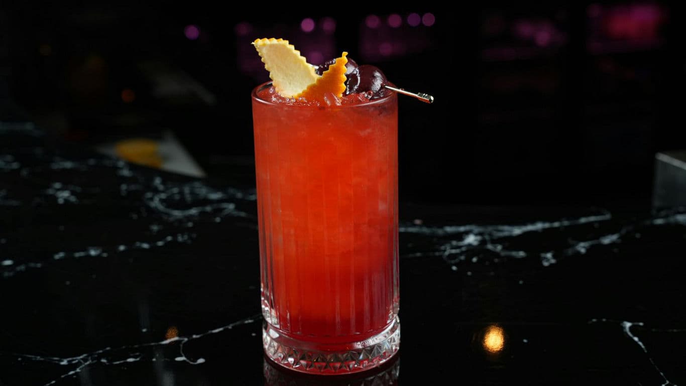 Vibrant red cocktail with citrus garnish on bar