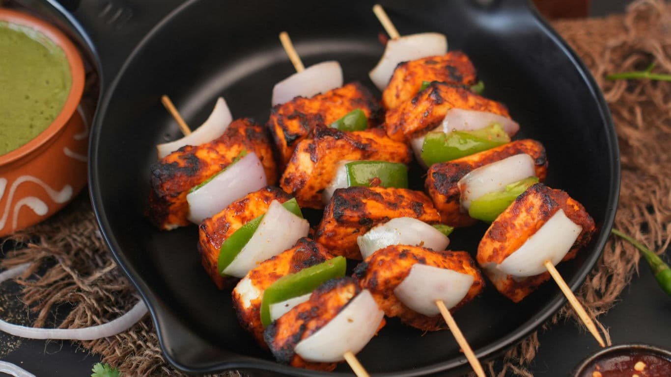 Grilled paneer tikka skewers with vegetables on plate