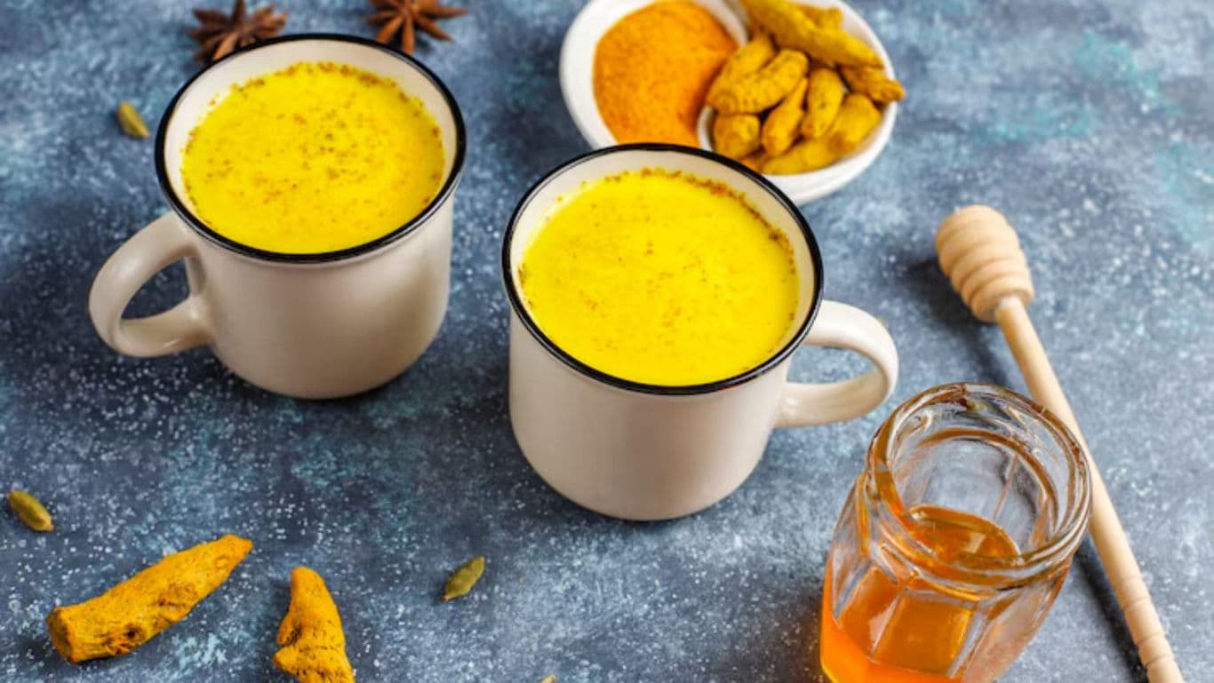 Two mugs of turmeric golden milk with honey and spices
