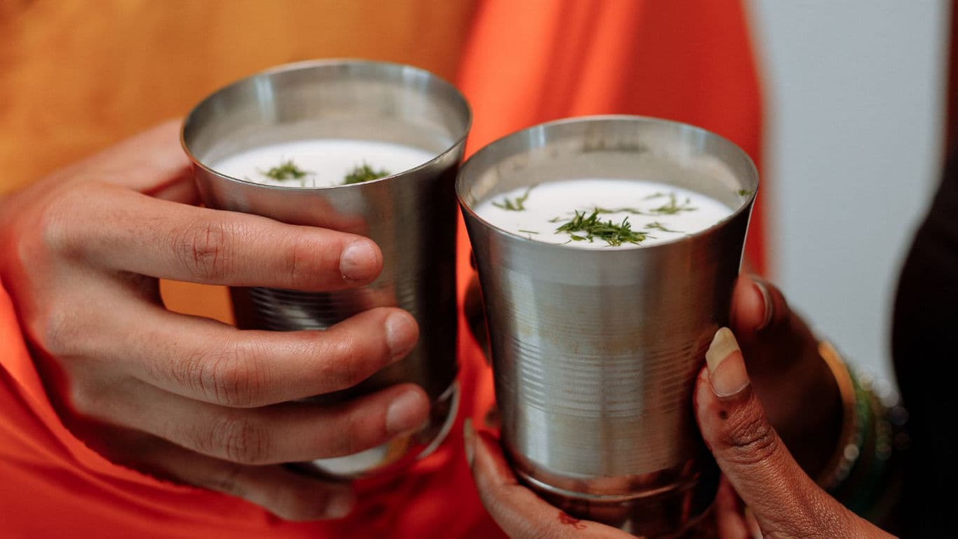 Two hands holding steel cups of buttermilk