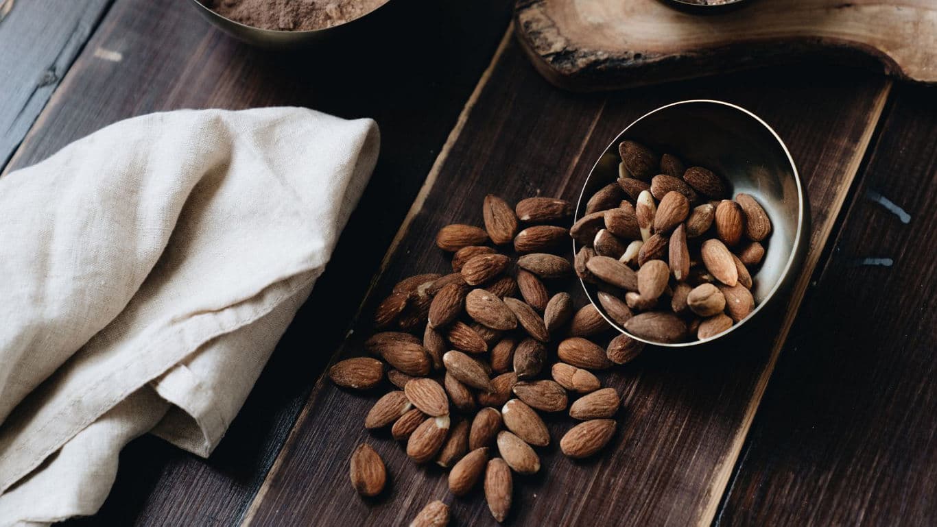 Raw almonds in metal bowls on rustic wooden table