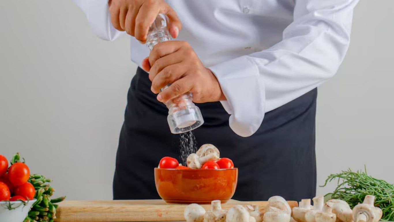 Chef seasoning fresh vegetables in bowl
