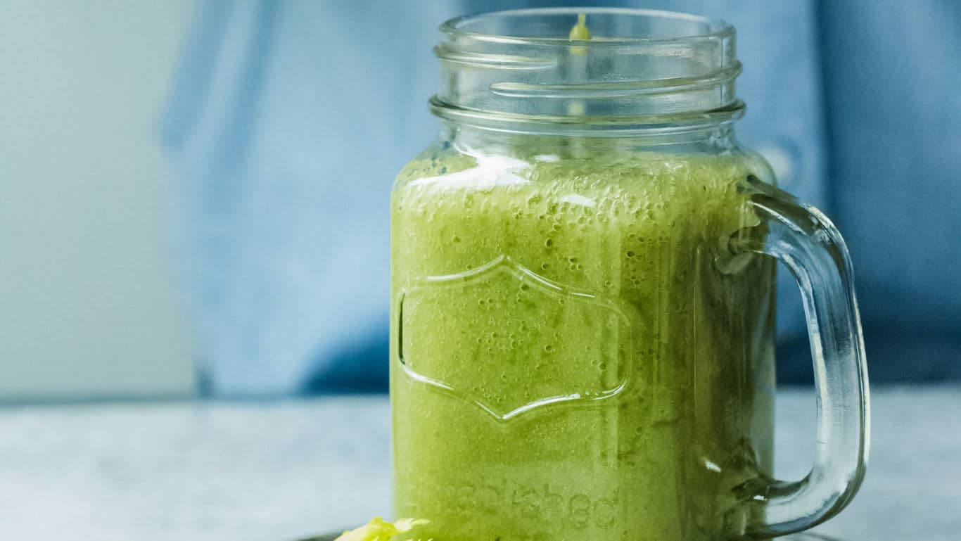 Green smoothie in mason jar on light surface