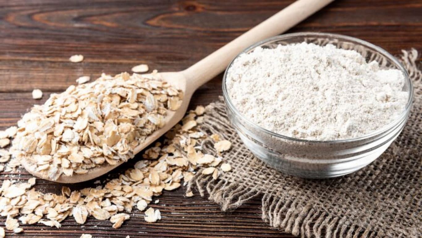 Wooden spoon with oats and bowl of flour