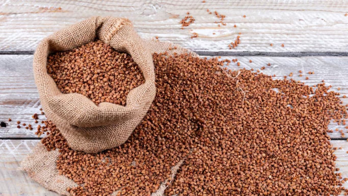 Buckwheat grains spilling from burlap sack on wood