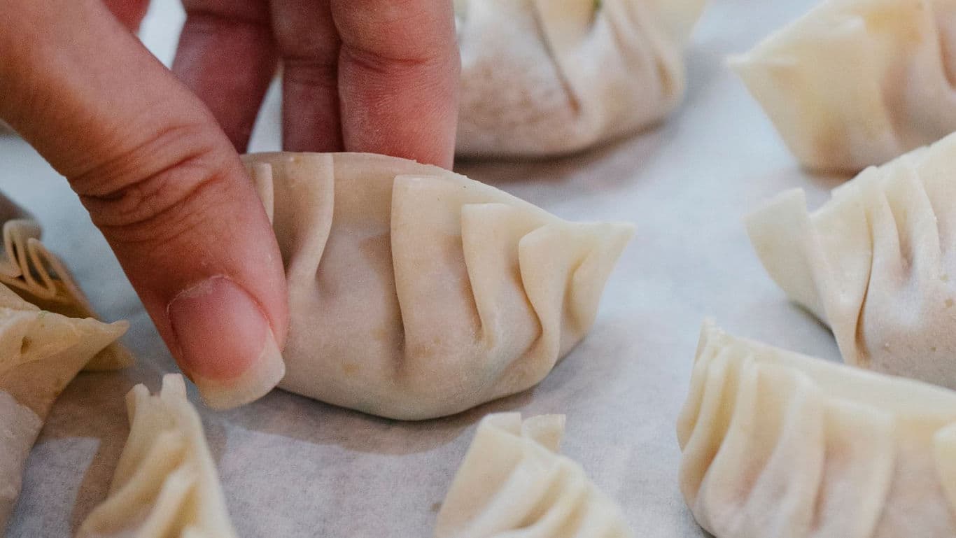 Hand folding fresh dumplings on parchment