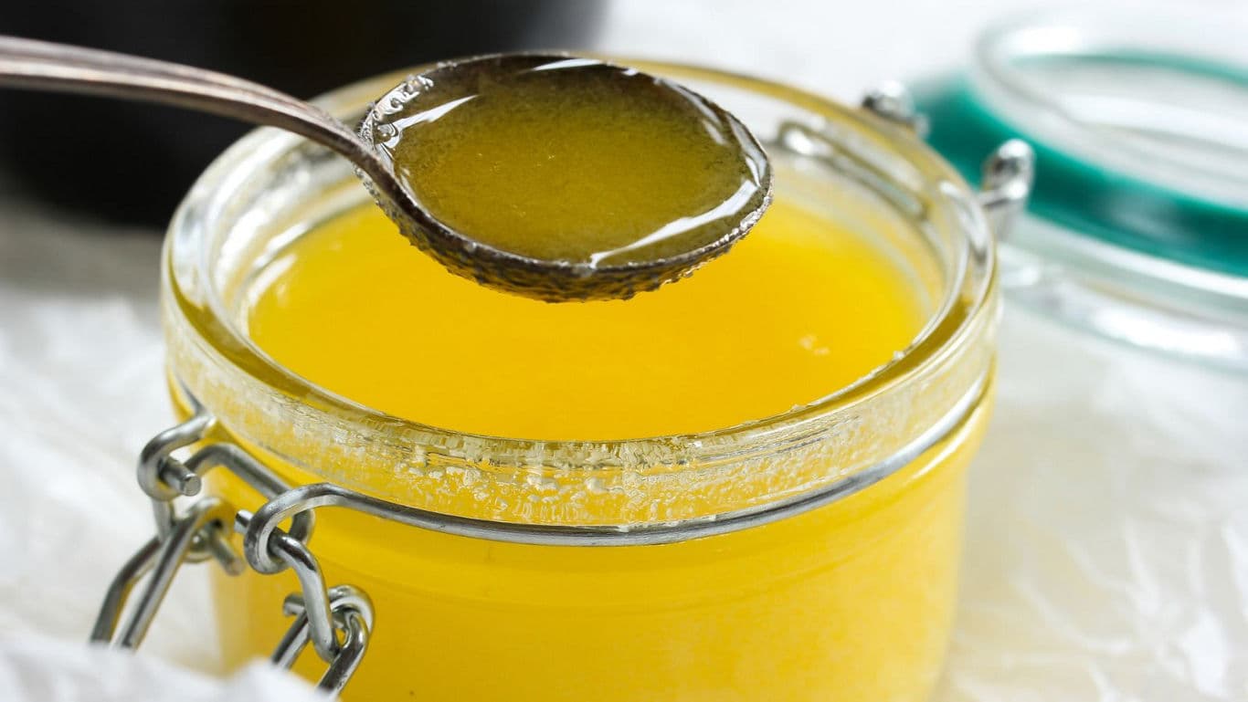Glass jar of clarified yellow ghee with spoon