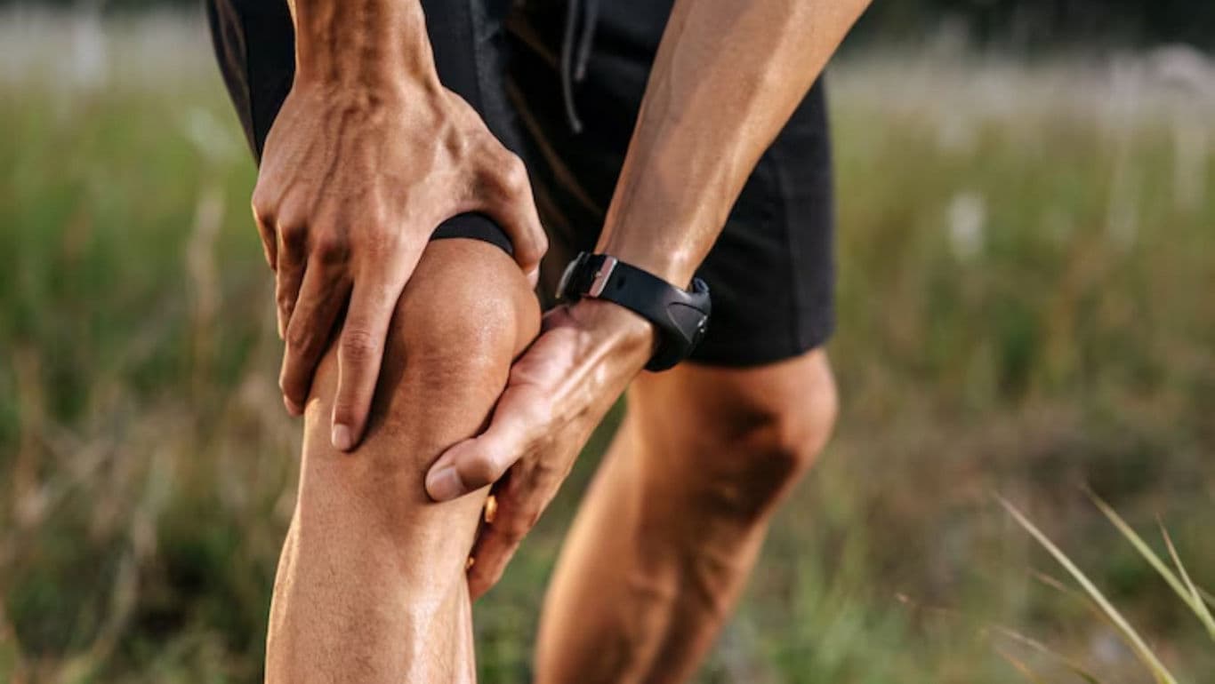 Runner holding knee in outdoor grassy field