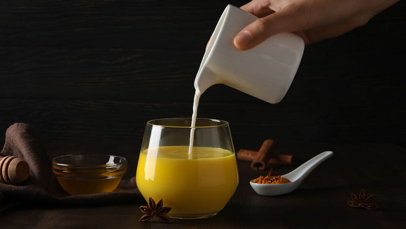 Hand Pouring Milk Into Turmeric Latte Glass