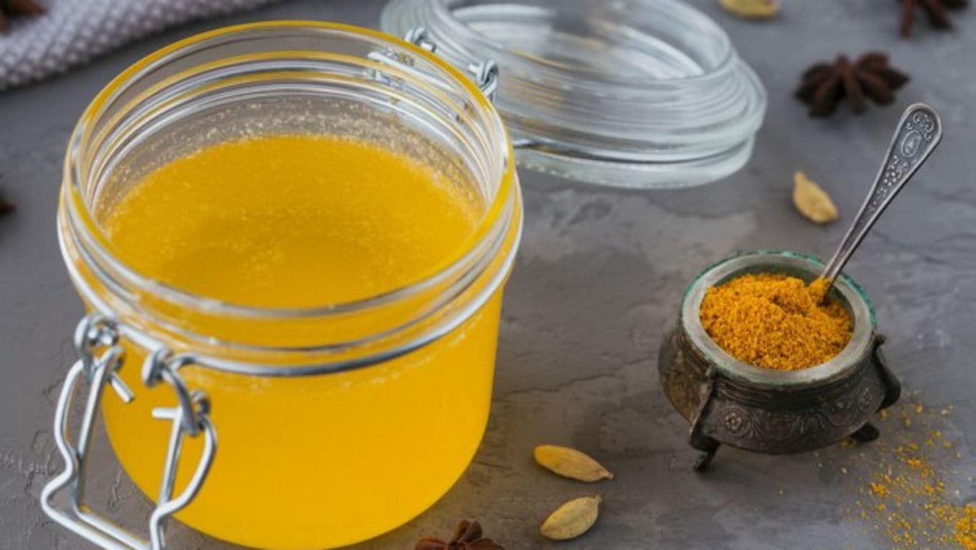 Glass jar of clarified yellow ghee with spices