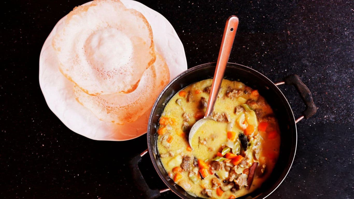 Traditional curry with appam on dark surface