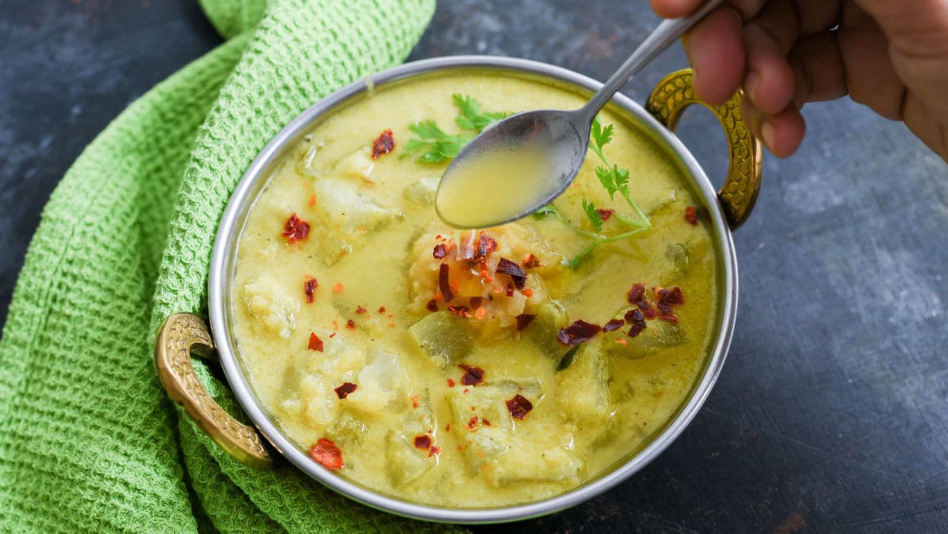 Hand serving hot vegetable soup in metal bowl