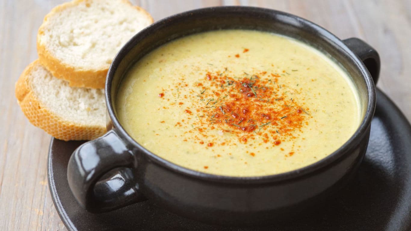 op-down view of a bowl of creamy mushroom soup with herbs and bread on the side