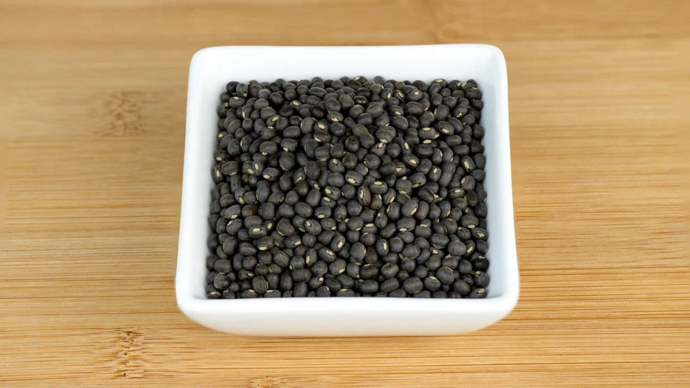 Close-up of raw black urad dal (whole black gram) with skin.