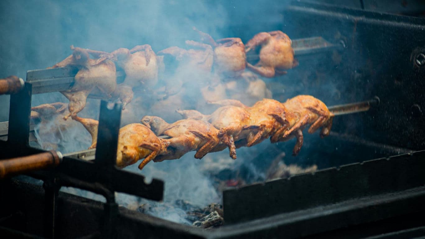 Whole chickens roasting on outdoor barbecue rotisserie
