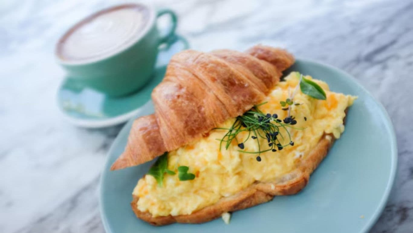 Scrambled egg croissant sandwich with hot beverage
