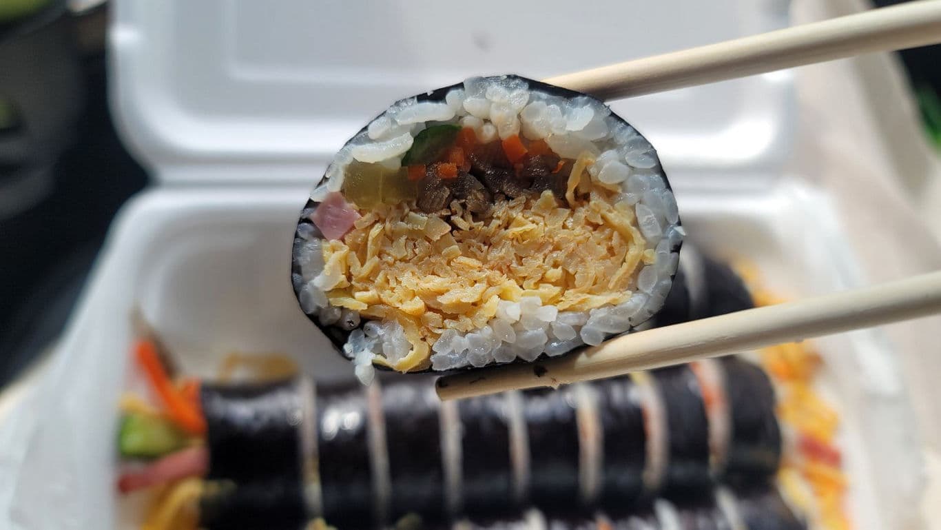 Close-up of kimbap roll held with chopsticks