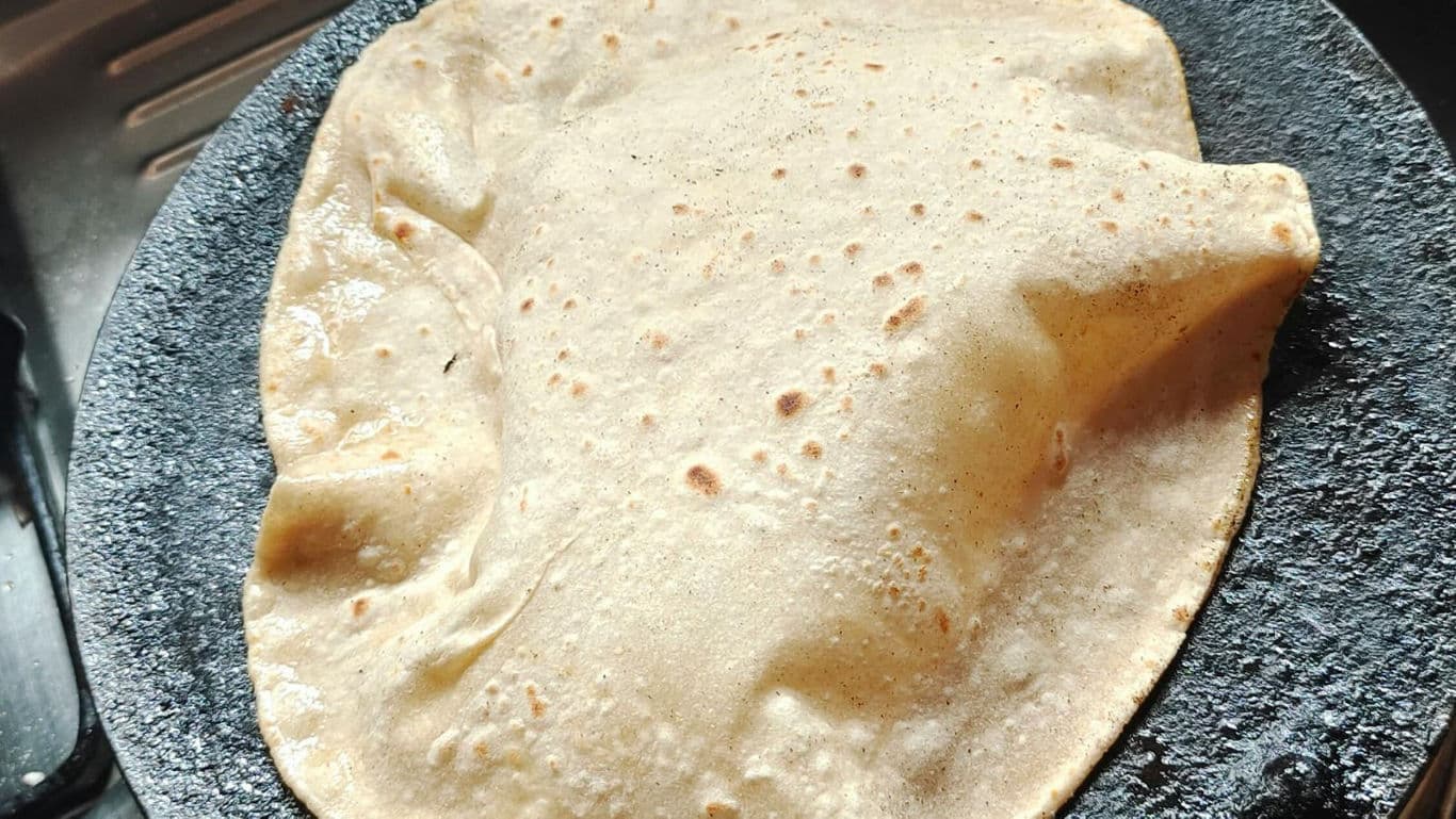 Freshly puffed roti cooking on hot griddle
