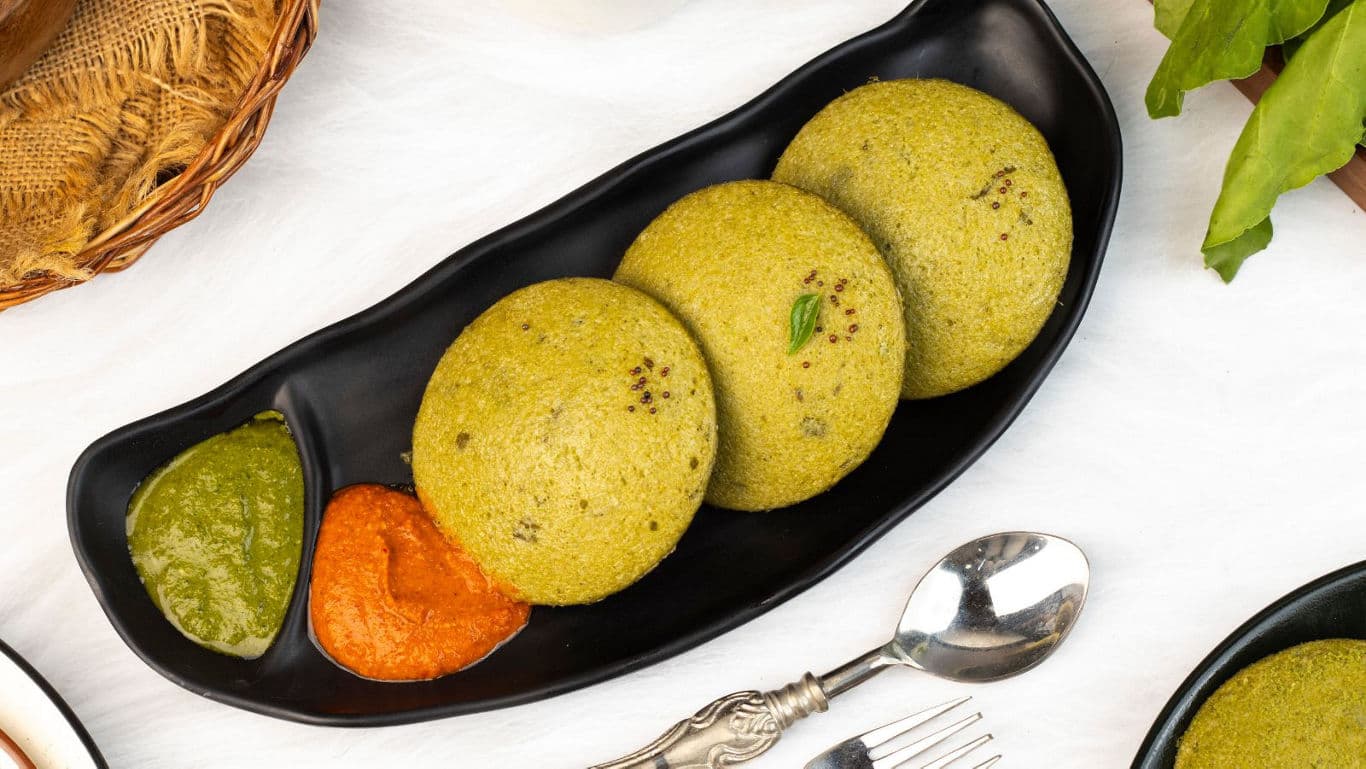 Green idlis with chutneys on black plate