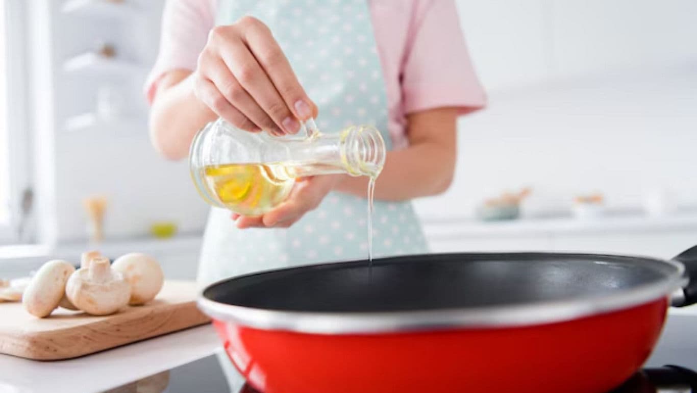 Person pouring oil into red frying pan in kitchen