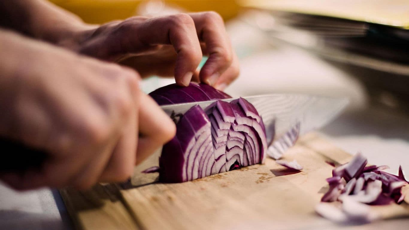 Slicing red onion on wooden cutting board