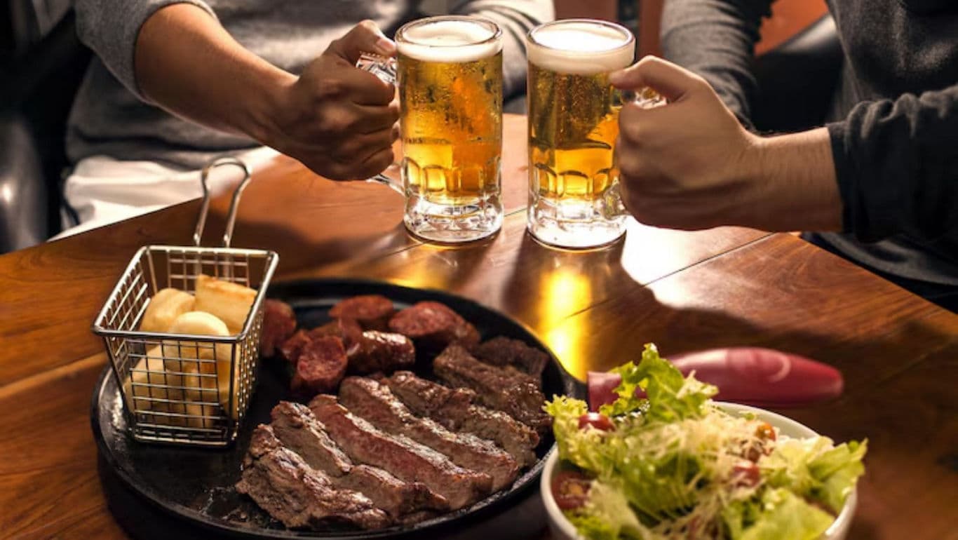Friends Toasting Beer Over Steak and Salad Dinner
