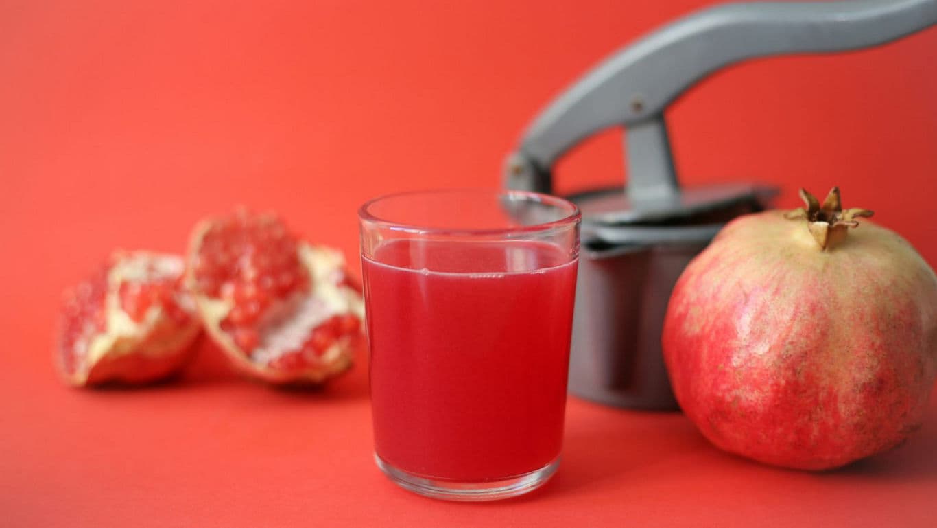 Fresh pomegranate juice with manual juicer on red background