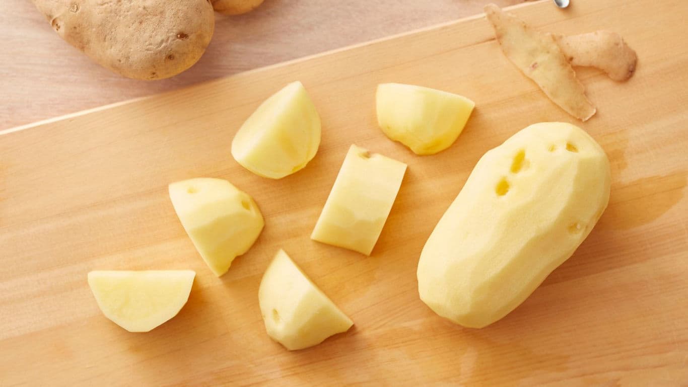 Peeled and chopped potatoes on wooden board
