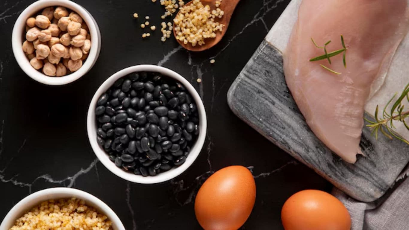 Raw chicken breast, eggs, beans, and grains on marble