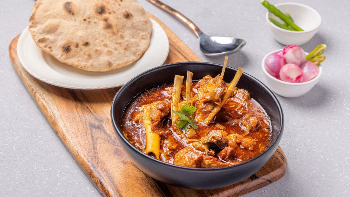 Spicy Indian mutton curry with roti and fresh sides