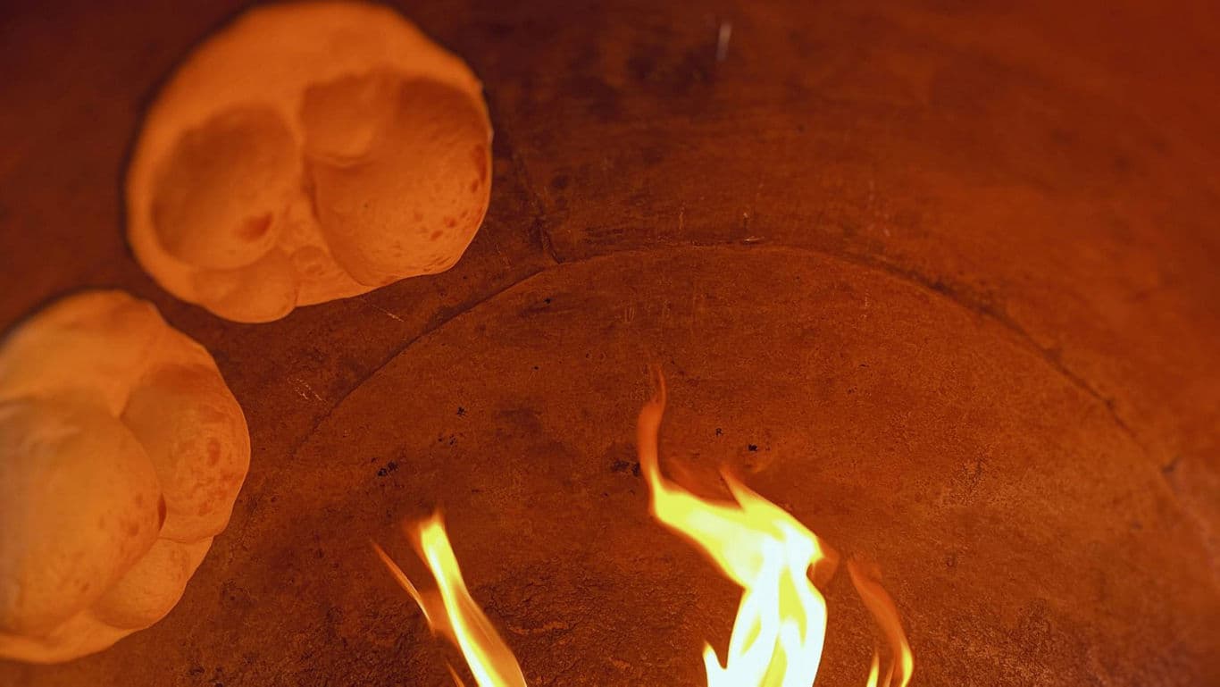 Traditional flatbreads baking inside clay tandoor oven