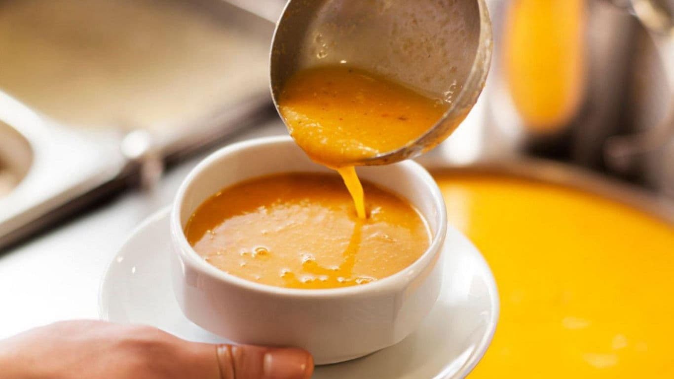 Ladle pouring orange soup into white bowl