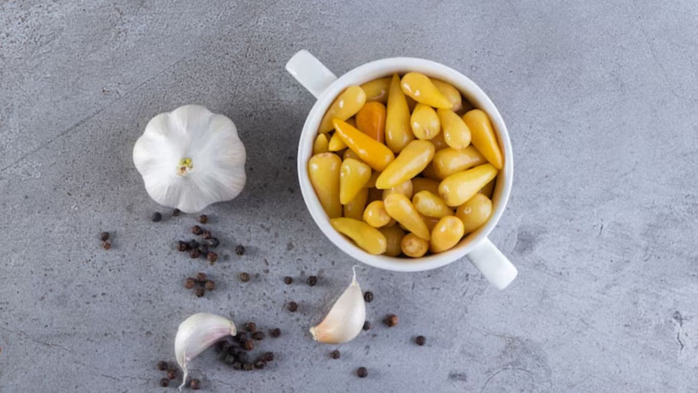 Yellow pickled peppers in bowl with garlic and pepper