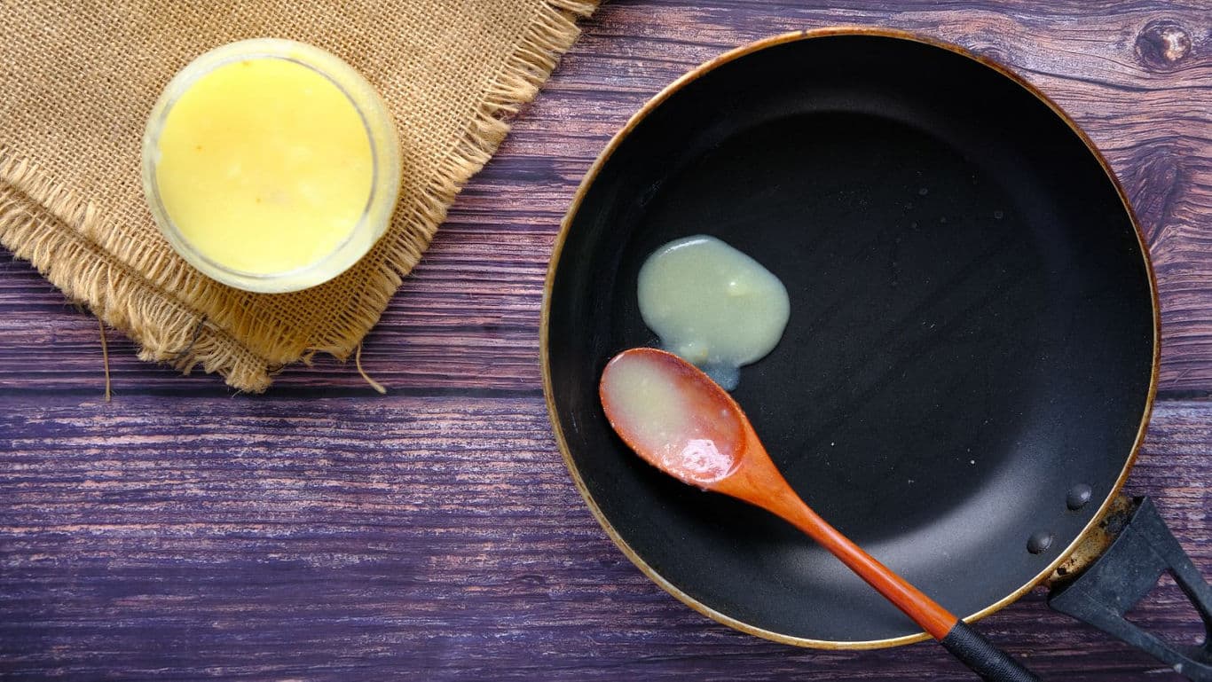Ghee melting in nonstick pan with wooden spoon