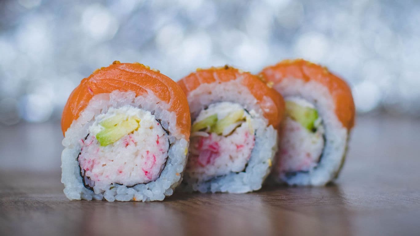Close-up of three salmon sushi rolls on wood