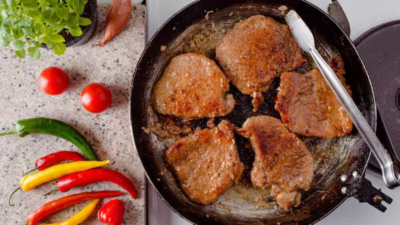 Six seasoned steaks cooking in frying pan overhead