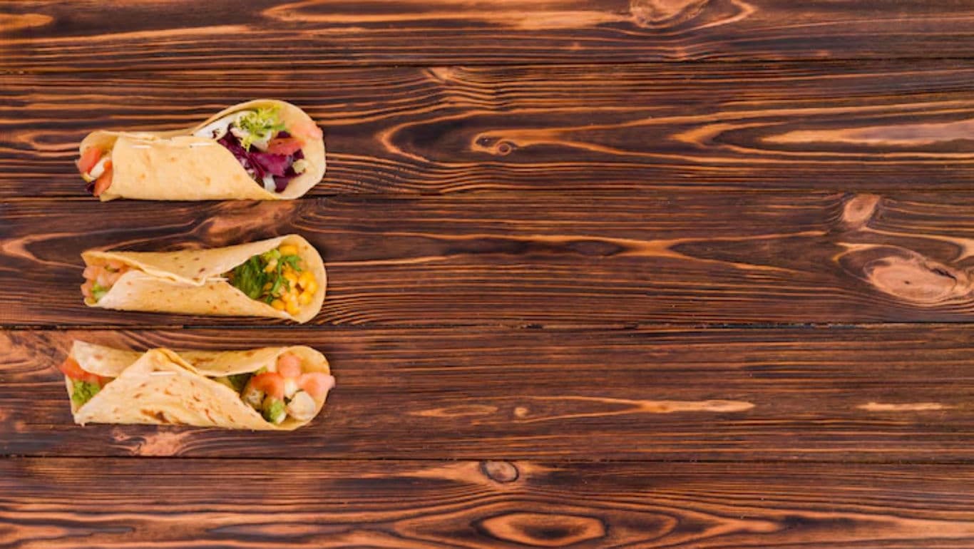 Three assorted tacos on rustic wooden table