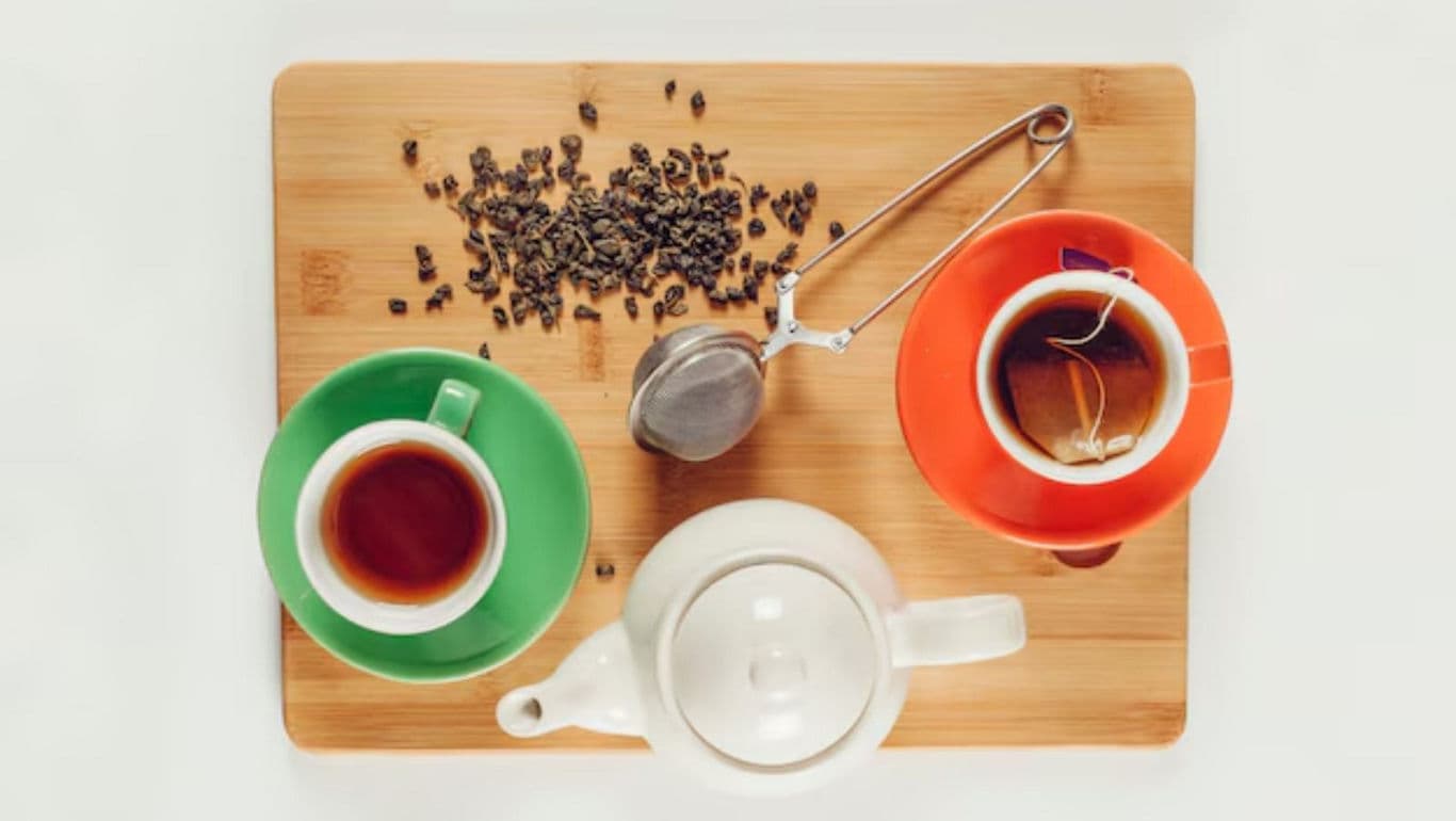 Tea cups and teapot with loose leaf tea on board