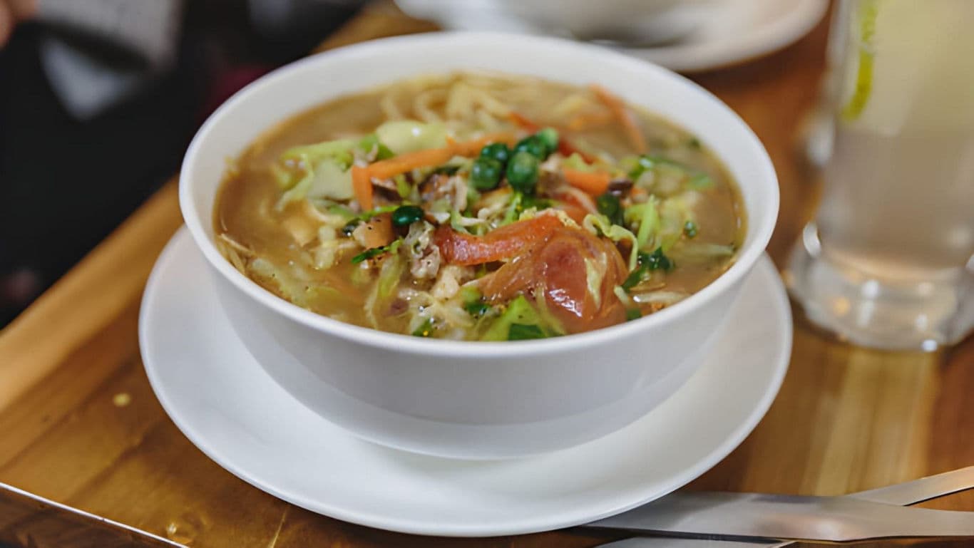 Steaming bowl of vegetable noodle soup on table
