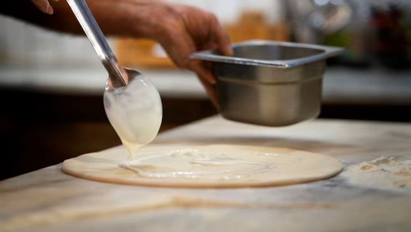 Chef Spreads Creamy Sauce on Pizza Dough in Kitchen