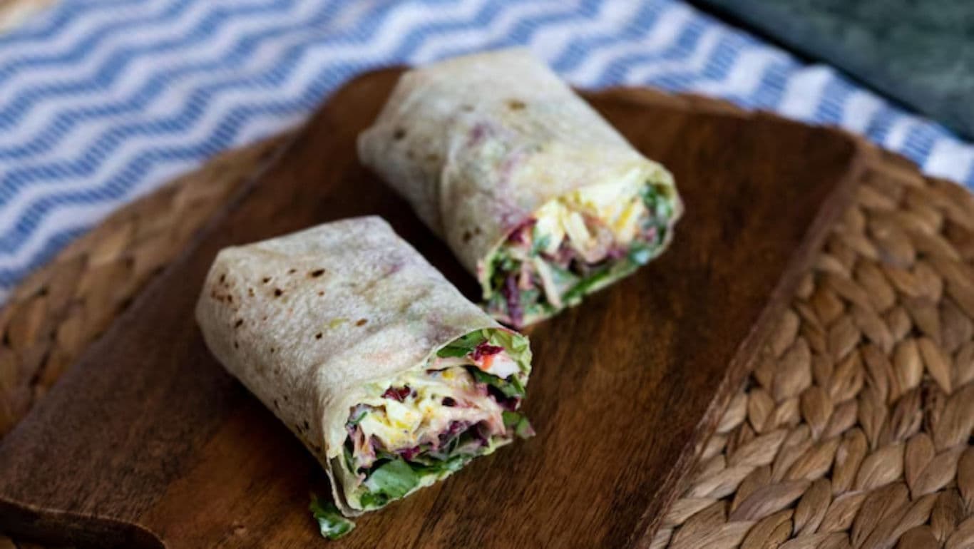 Fresh vegetable wrap cut in half on board