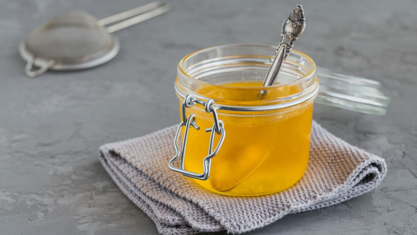 Glass jar of golden honey with silver spoon
