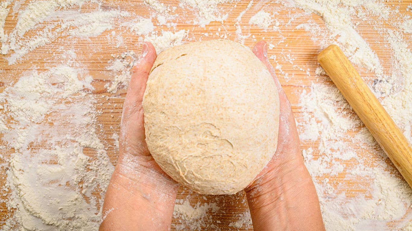 Hands Shaping Fresh Dough on Floured Surface