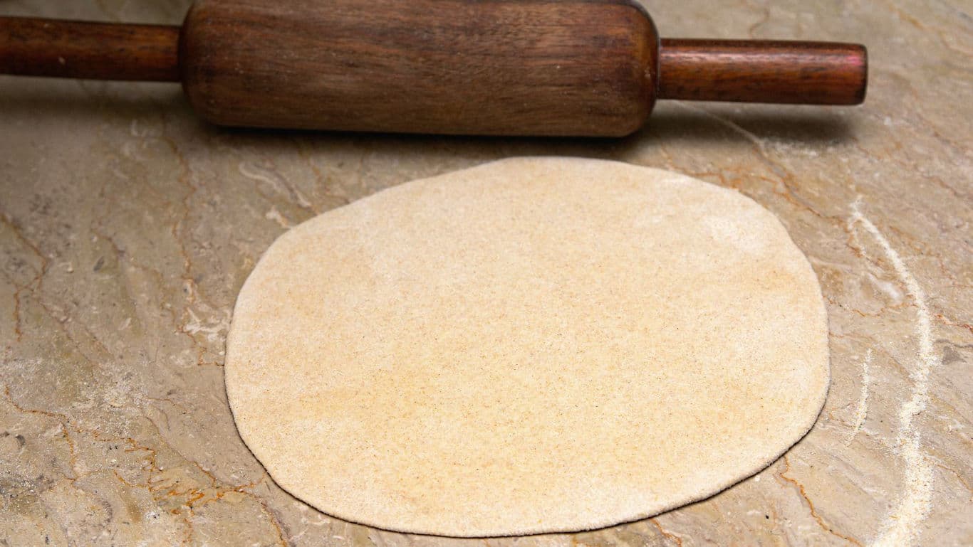 Rolled dough with wooden rolling pin on countertop