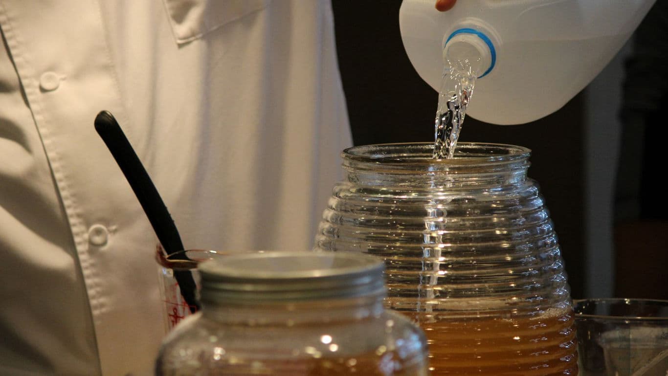 Person pouring water into large glass jar in kitchen