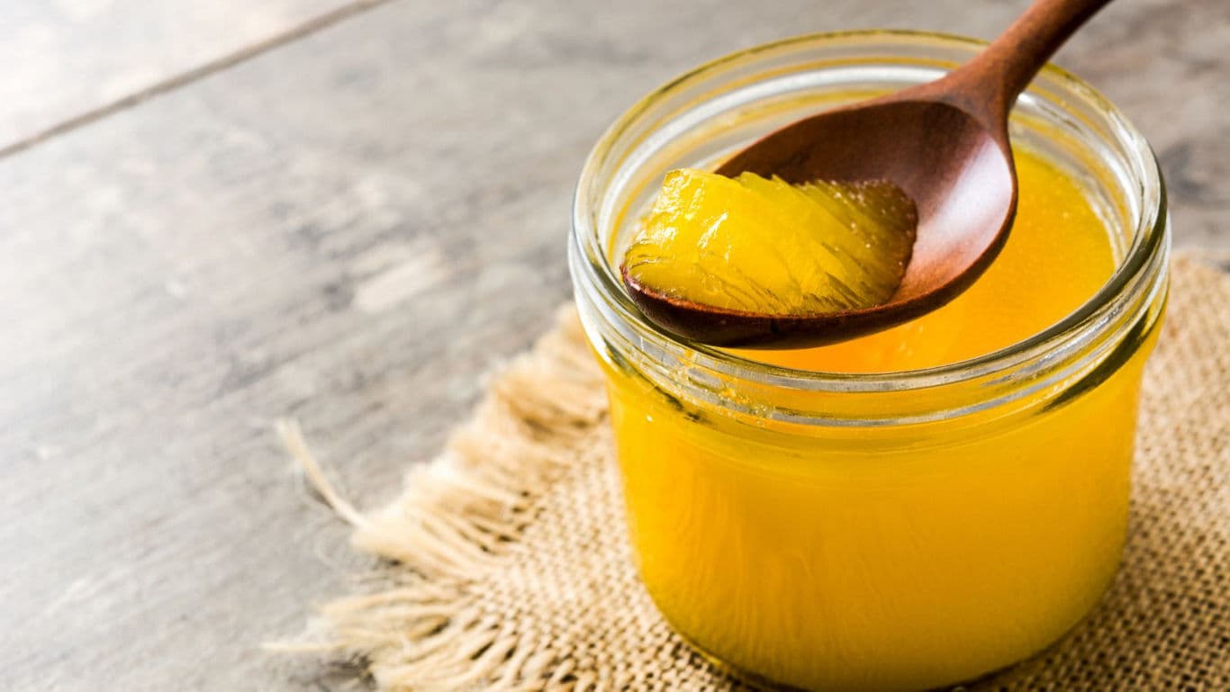 Glass jar of yellow clarified butter on rustic table